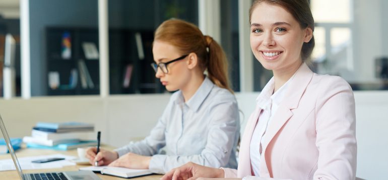 Two women sitting at a table with laptops.