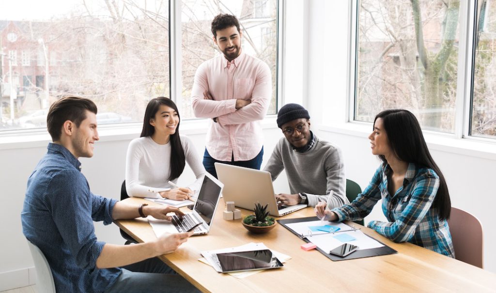 A group of people sitting around a table with laptops.